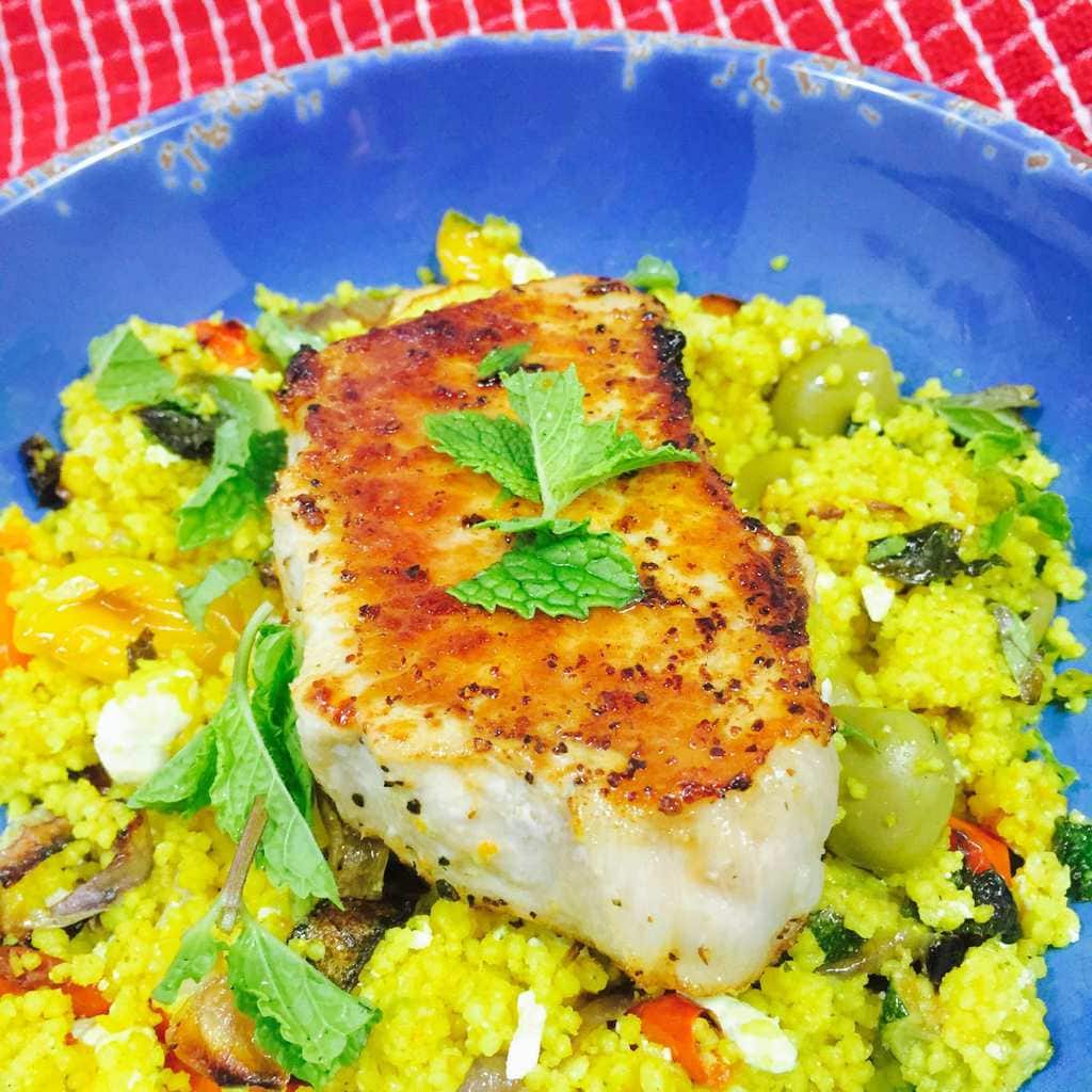 Baked pork chop resting on curry vegetable couscous on a blue plate.