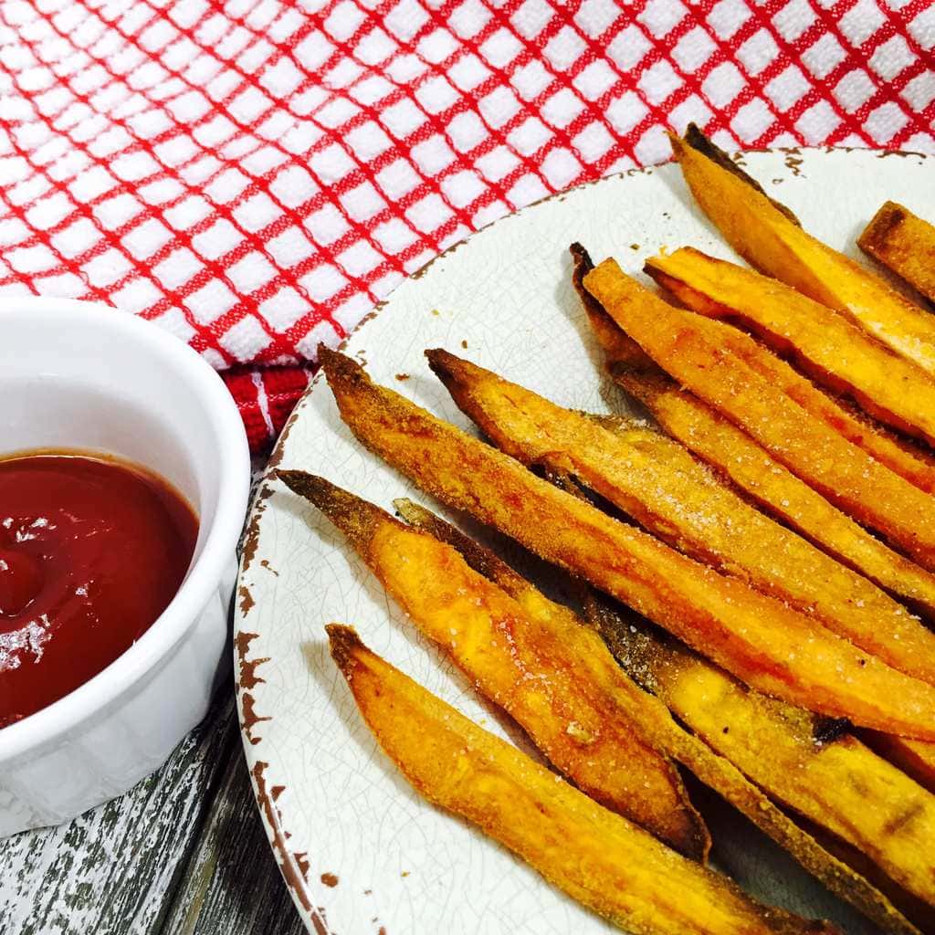 Sweet potato fries on a white plate along side ketchup in a white bowl