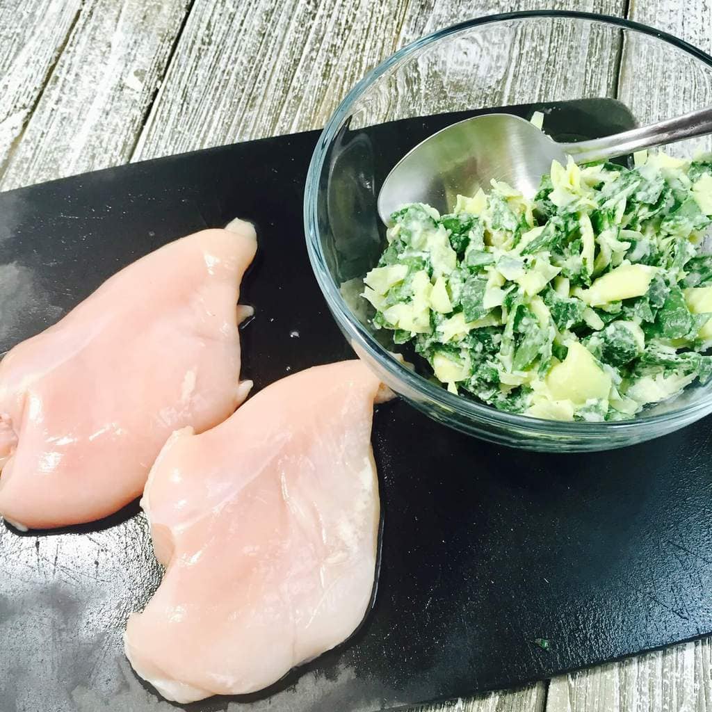 Uncooked chicken breasts and spinach stuffing on a cutting board