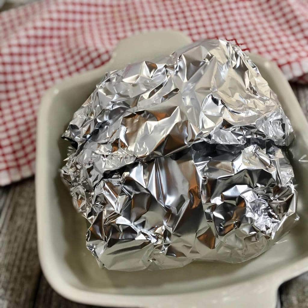 Brisket wrapped in foil in a white dish