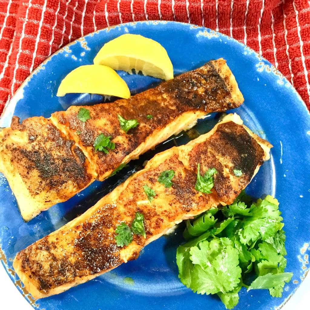 baked salmon on a blue plate with lemons and parsley